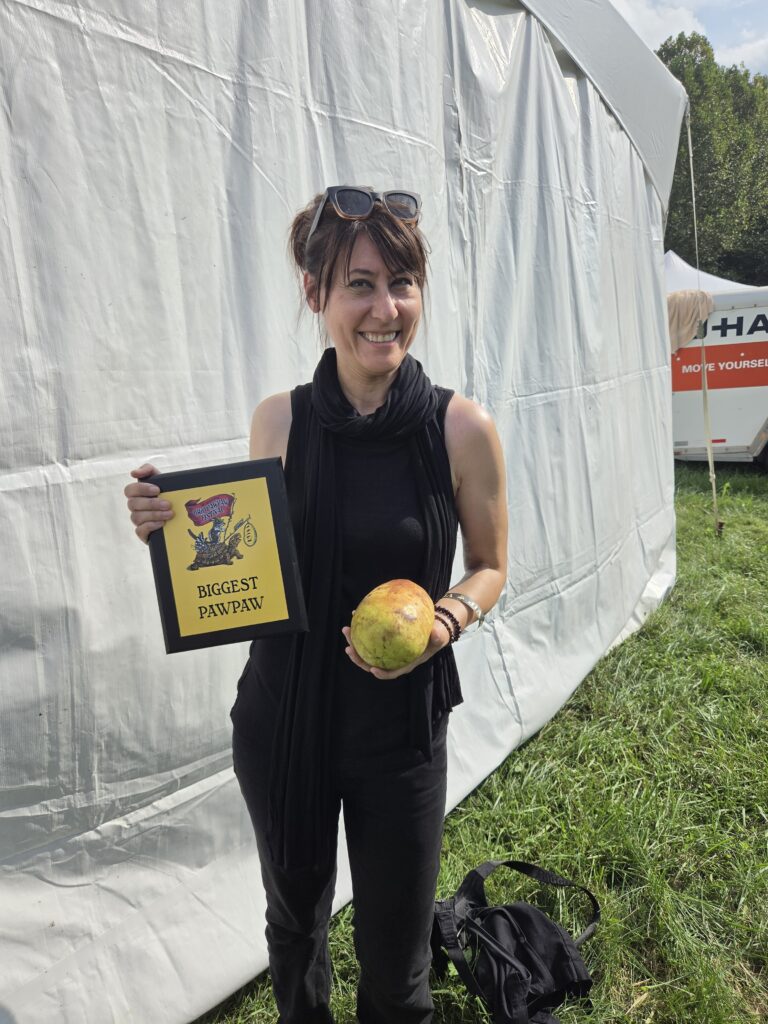 Valerie Libbey holding her Biggest Pawpaw award and winning Susquehanna pawpaw at the 2026 Ohio Pawpaw Festival